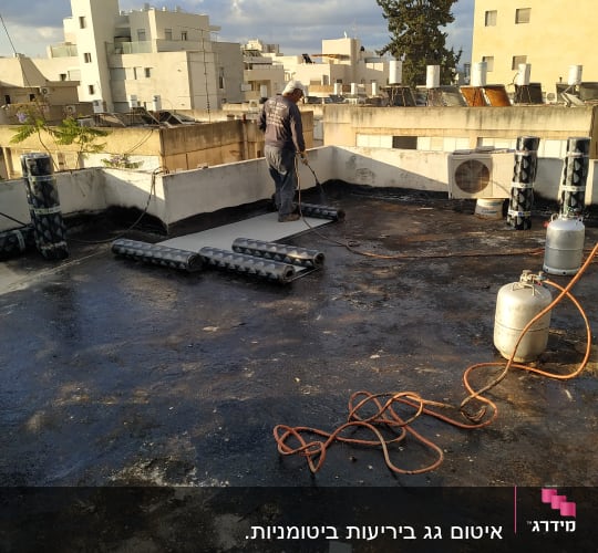 אדם אוטם גג עם יריעות ביטומניות ומבער גז
